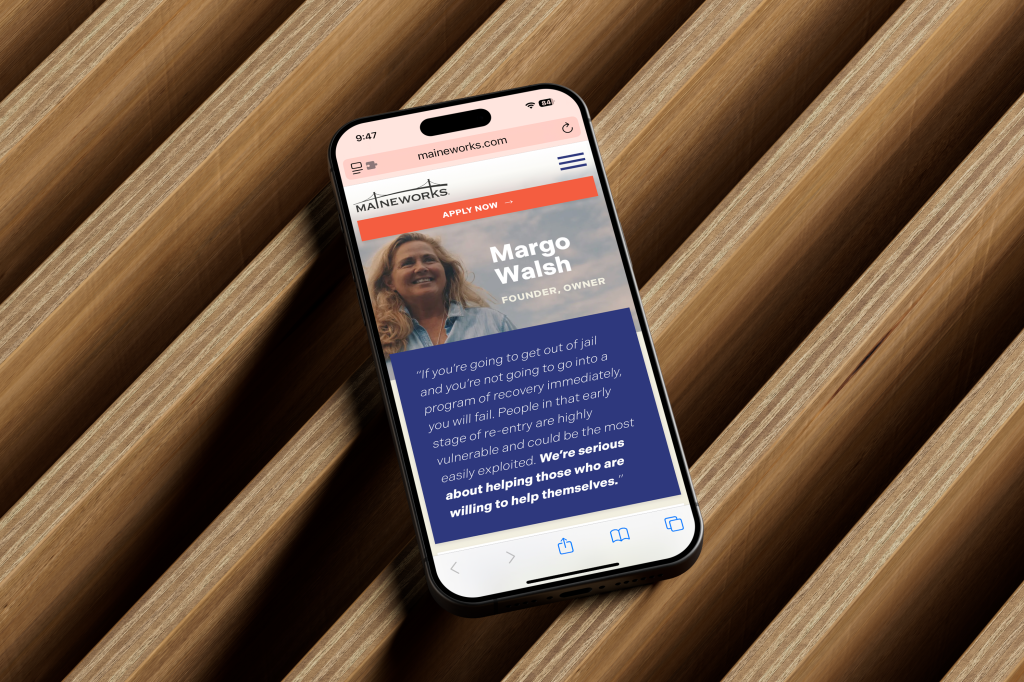 an iphone laying across wooden slats, displaying a profile page for Margo Walsh on the MaineWorks website